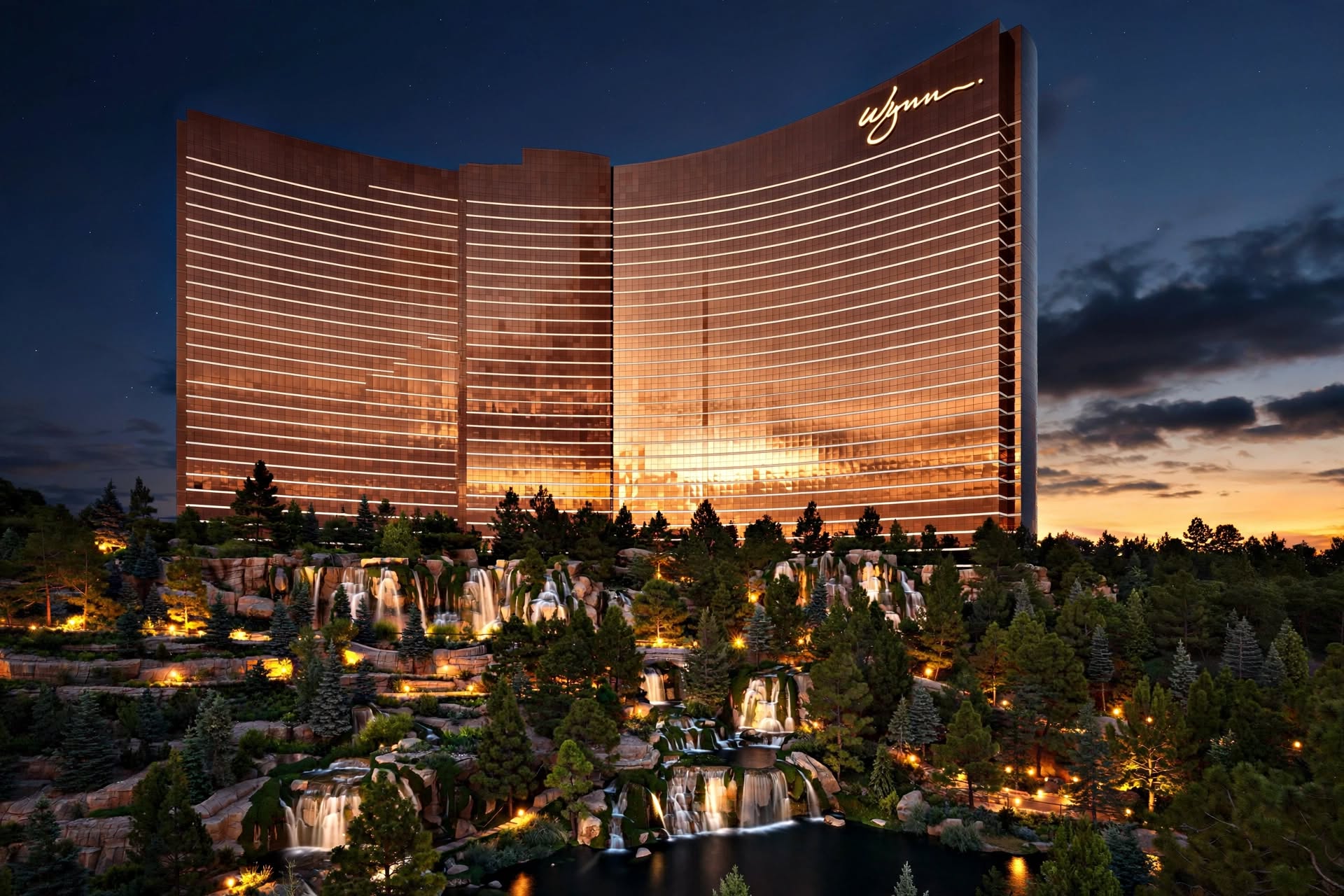 Curved bronze reflective glass resort tower rising above lush landscaped hillside waterfalls